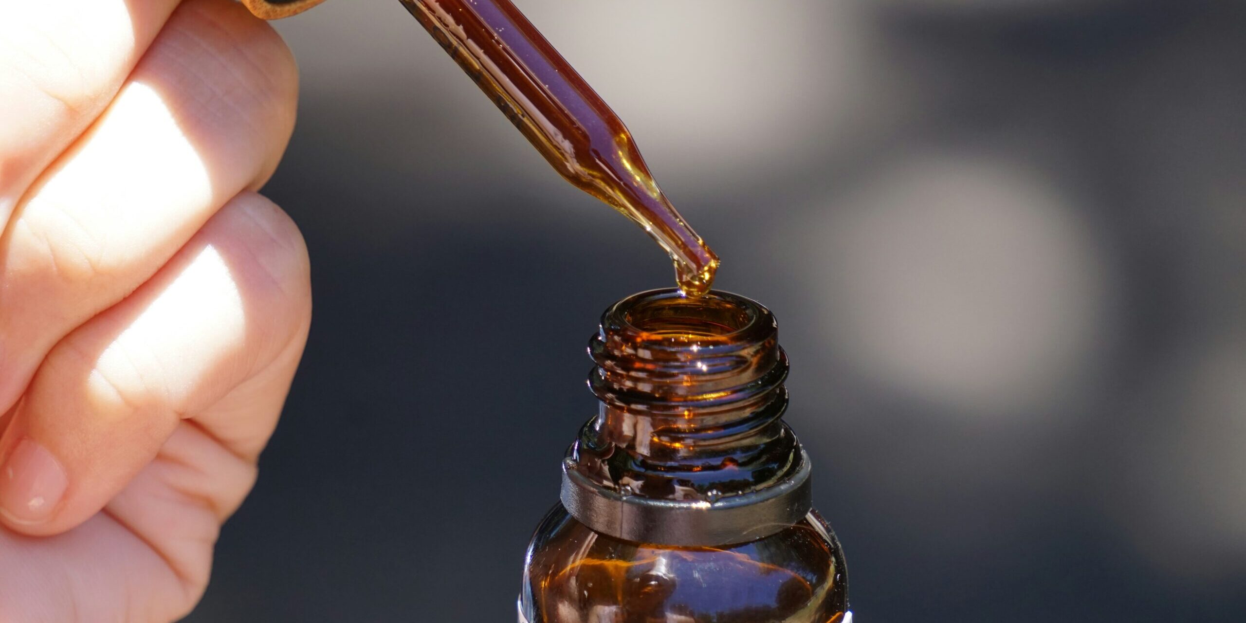 Close-up of a hand holding a dropper above a brown glass bottle, dispensing cannabis tincture oil for pain relief.